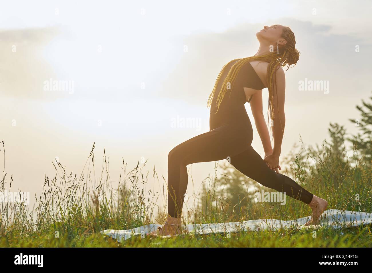 Side view of sporty woman practicing yoga. Young female stepping with one leg forward, bending with hands in lock, looking at sky. Concept of harmonic Stock Photo