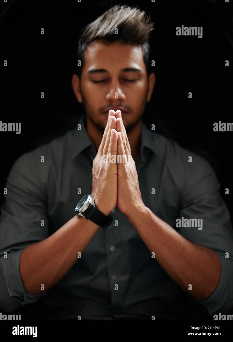 Counting his blessings. Shot of a focused young man standing with his hands together and praying with his eyes closed. Stock Photo