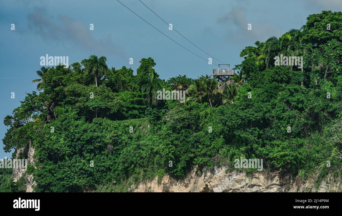 The photo shows a zip line. It is located on a high mountain peak. Green spaces grow on the rock. Gray clouds are visible in the blue sky. The extreme Stock Photo