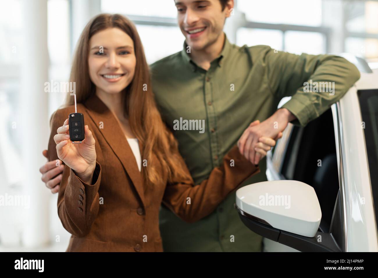 Happy young Caucasian couple showing key to their new car at automobile ...