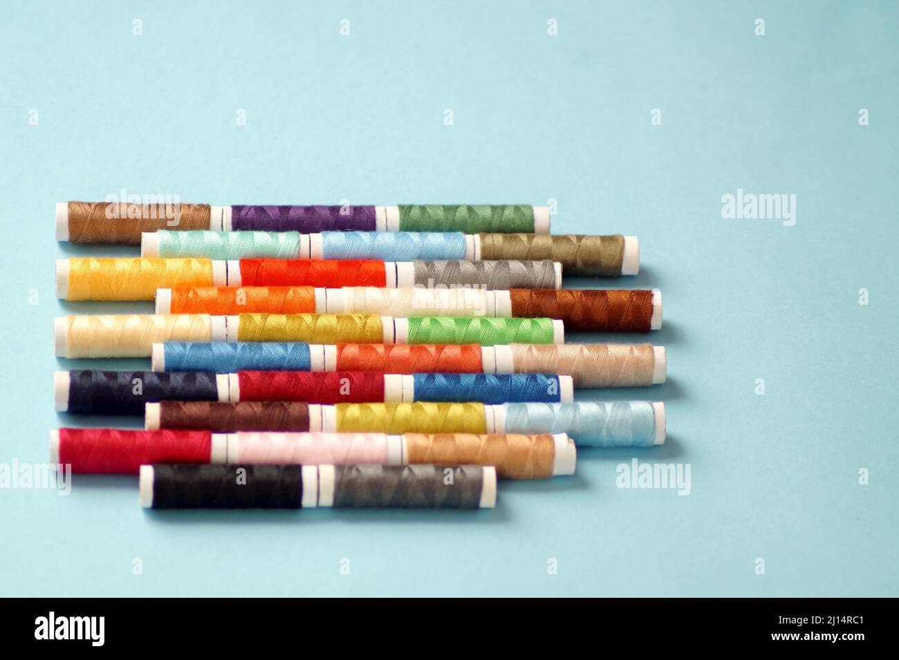 spools of colored thread lie in horizontal rows on a blue background Stock Photo