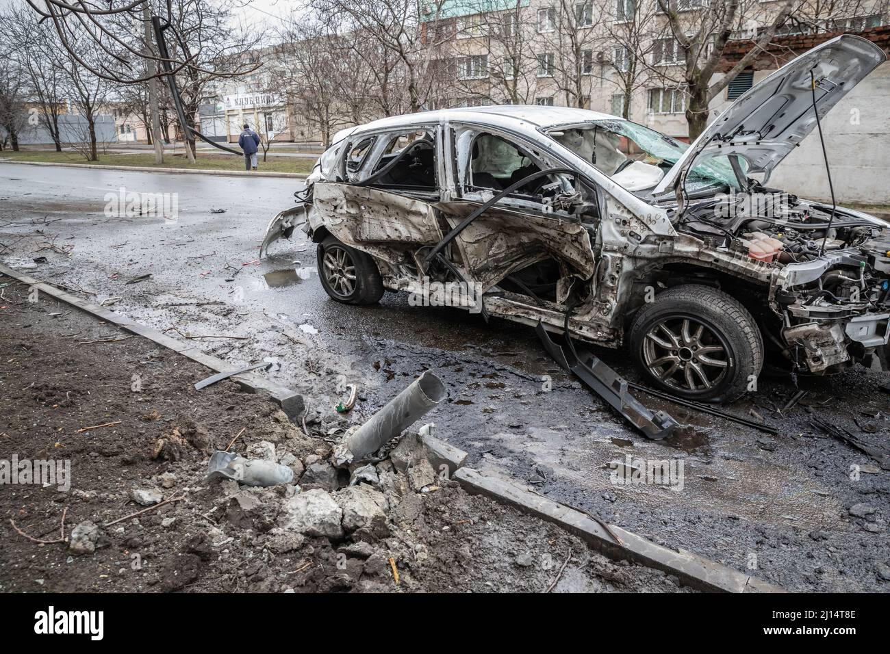 Remains of a Grad missile embedded in the ground and a damaged car parked in a street aftermath of Russian shelling in Mariupol, Ukraine, during the R Stock Photo