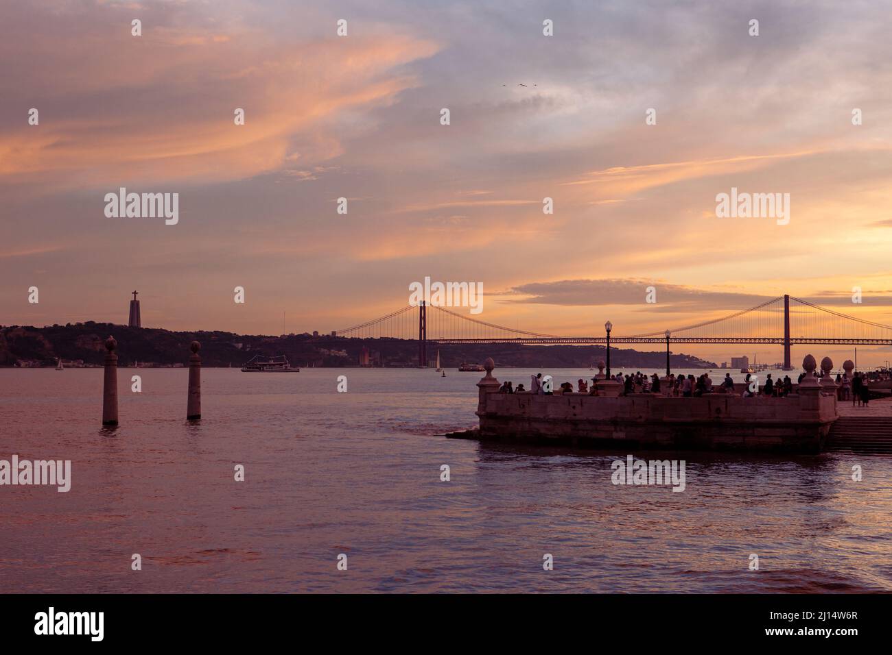 Tourists enjoying the sunset at Cais das Colunas pier, on the banks of the Tejo in Lisbon, with the Ponte de 25 Abril in the background, Portugal. Stock Photo