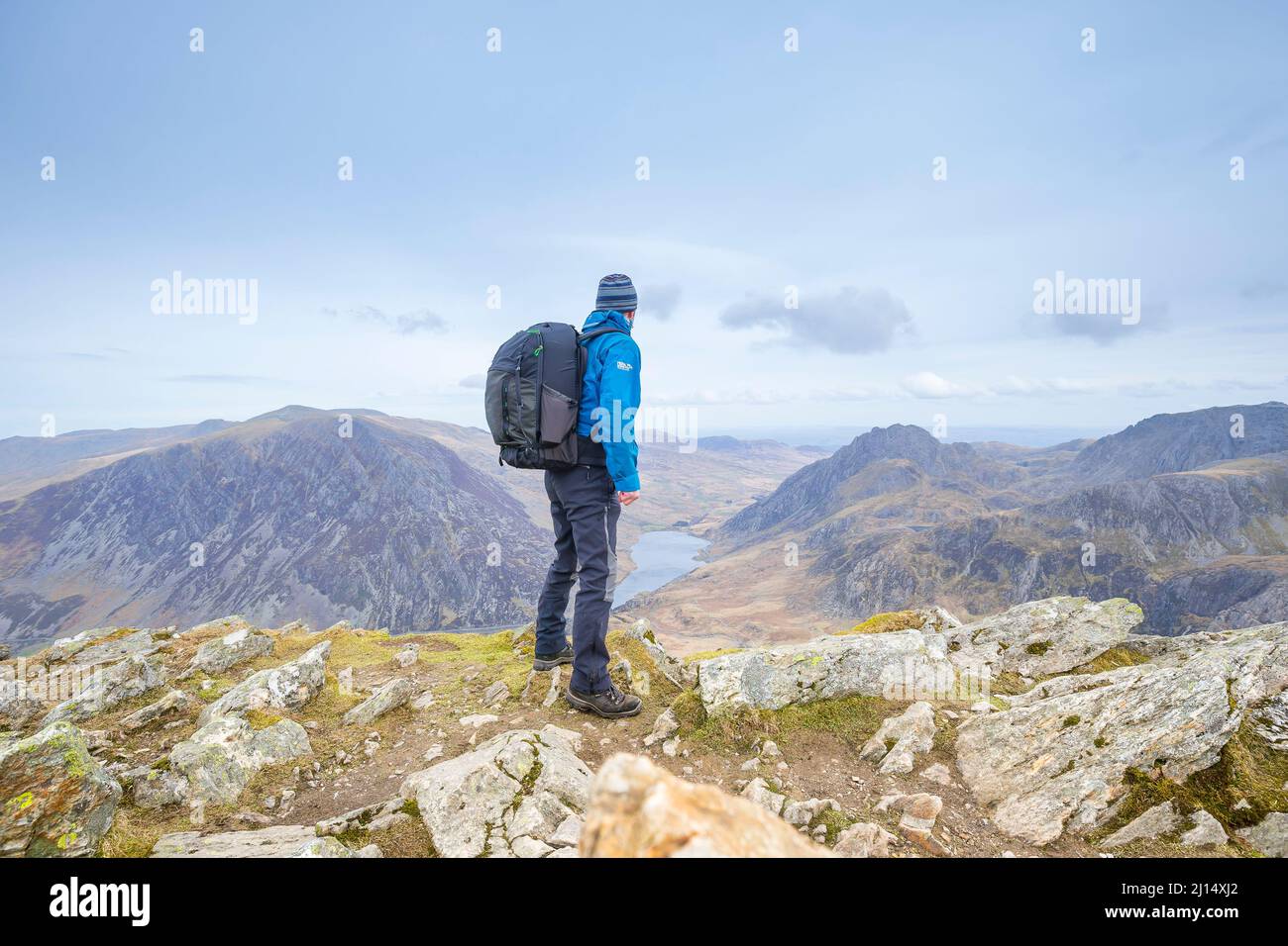 Rear view of isolated male backpacker hiking mountains in Snowdonia National Park, North Wales, UK, looking at landscape scenery on wild camping trip. Stock Photo