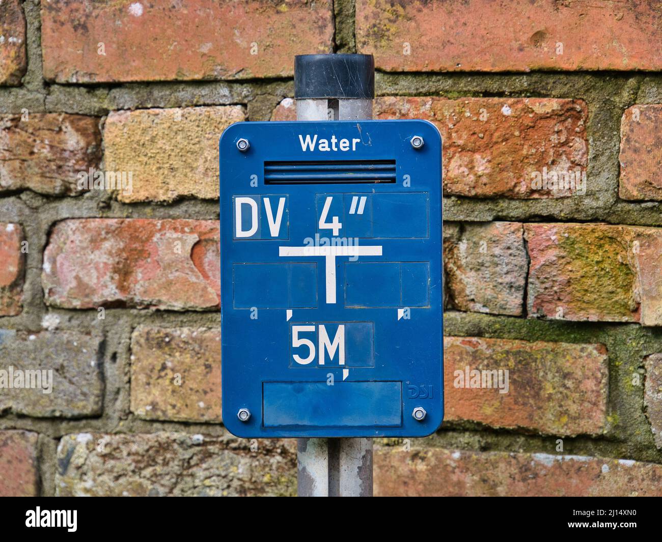 A blue, rectangular sign on a metal post indicates the location of buried water supply pipes. Stock Photo