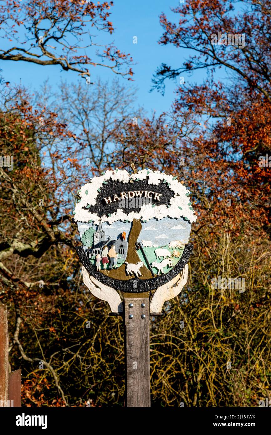 The traditional village sign for Hardwick shows hands holding the church, villagers and a small herd of sheep and lambs, Cambridgeshire, UK. Stock Photo