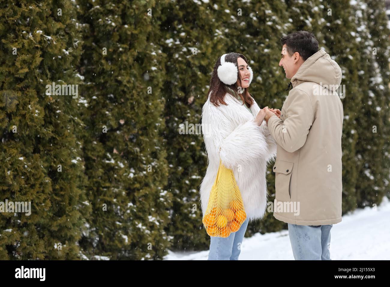Loving couple with oranges in string bag holding hands on snowy winter day Stock Photo