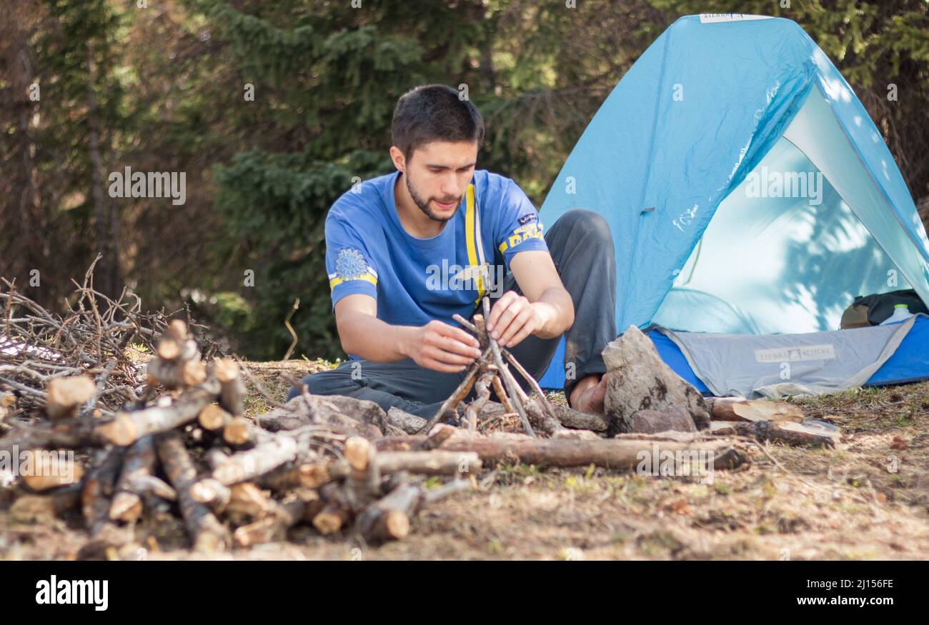 Outdoorsy hispanic man building a fire at a campsite in the woods Stock Photo