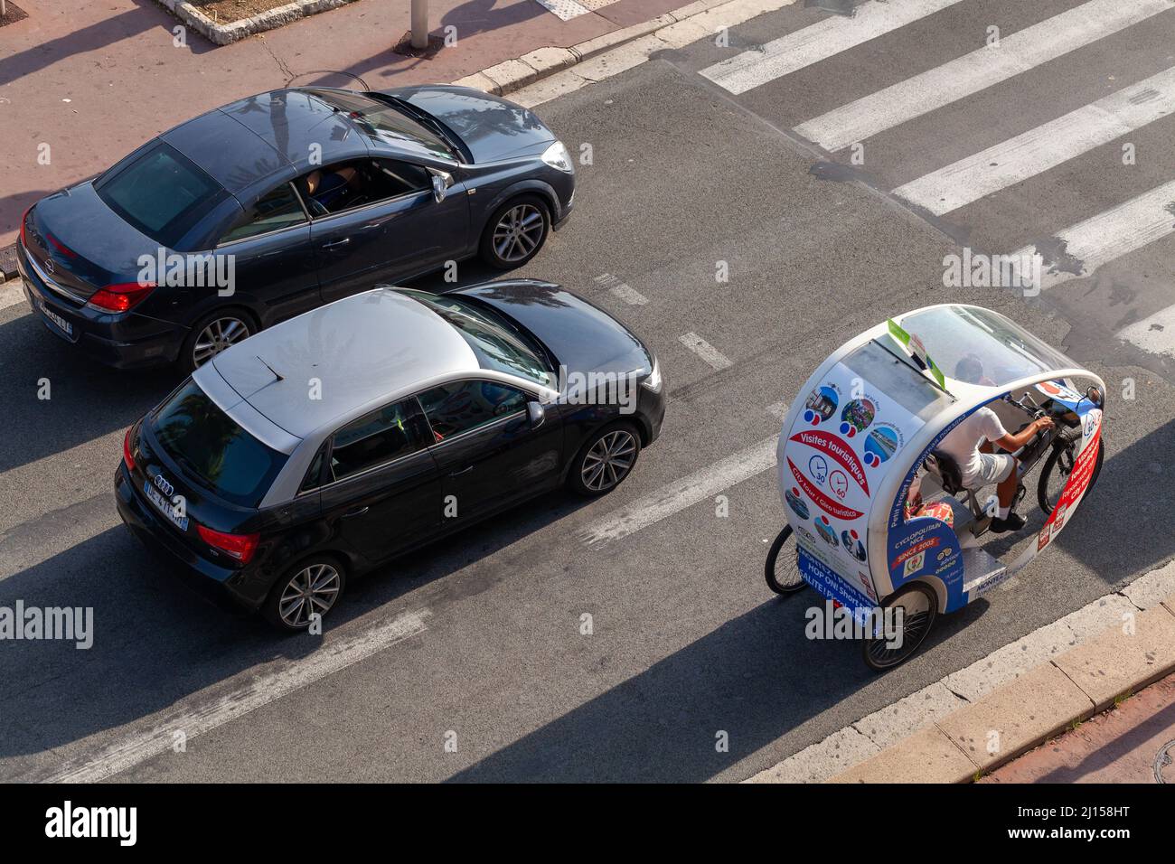 Nice, France - August 13, 2018: Cars and tourists trishaw bike are on the road on a sunny day Stock Photo