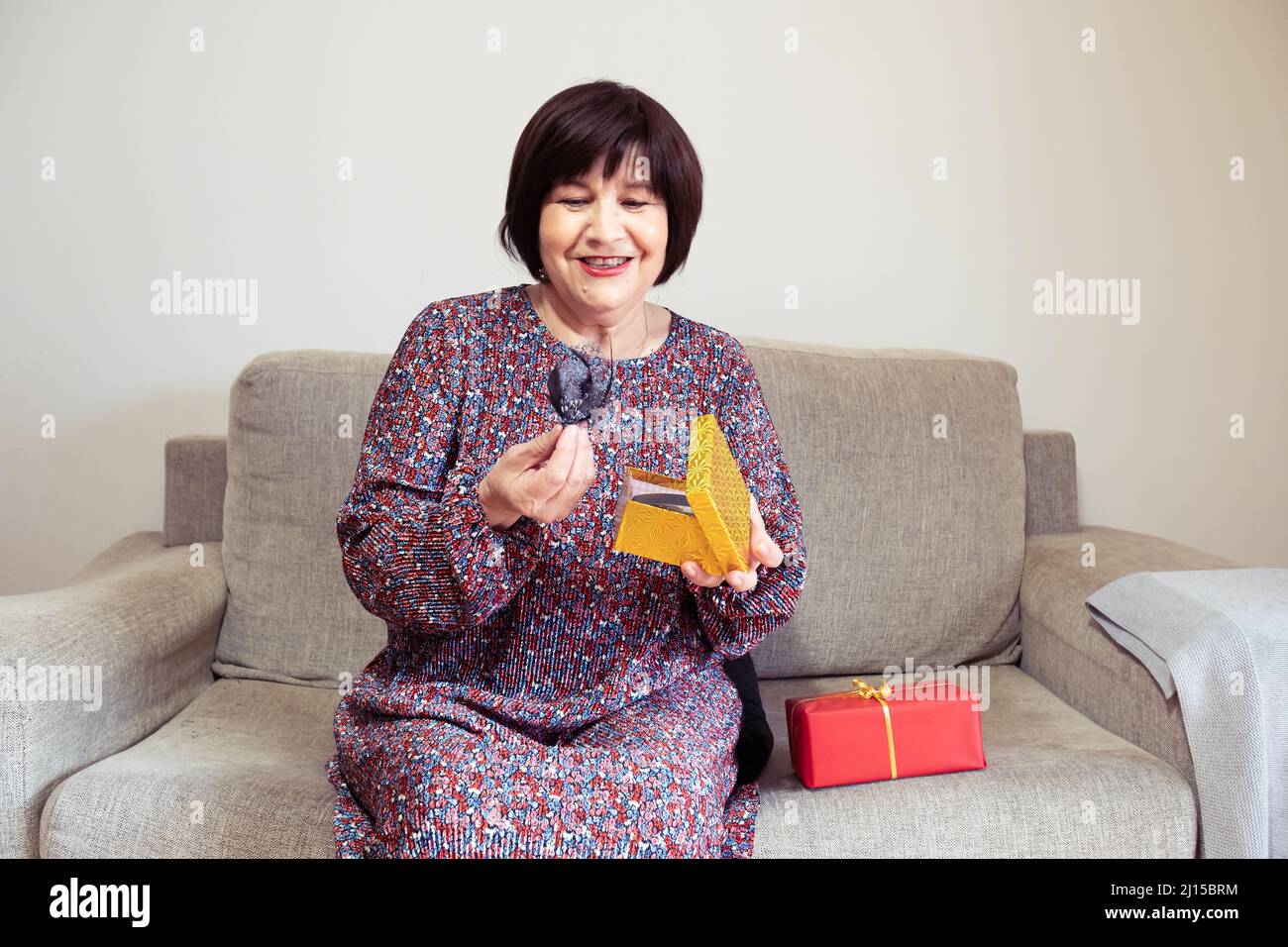 Grandma opens a present on her sofa and has a second present waiting Stock Photo