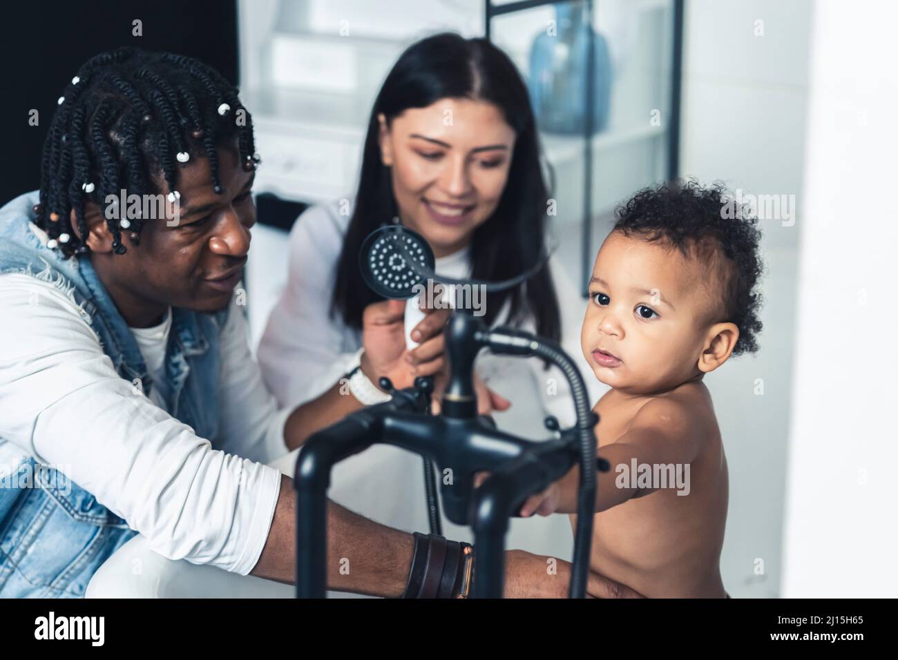 Multiracial parents learn their adorable curly-haired toddler to use a shower. Bath time. High quality photo Stock Photo