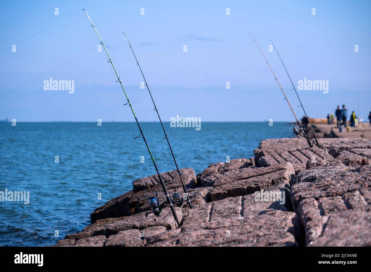 Fishing rods and reels in Port Aransas, Texas on popular jetty at the Gulf of Mexico with waves on the water. Stock Photo