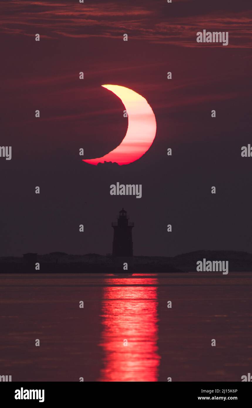 A partial solar eclipse is seen as the sun rises behind the Delaware Breakwater Lighthouse, Thursday, June 10, 2021, at Lewes Beach in Delaware. The annular or “ring of fire” solar eclipse is only visible to some parts of Greenland, Northern Russia, and Canada. Photo Credit: (NASA/Aubrey Gemignani) Stock Photo
