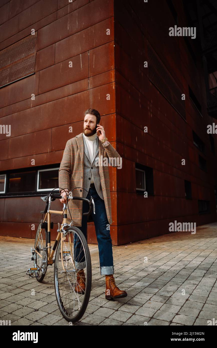 Young man with bicycle going to work. Calling with manager. Creative businessman in a modern business area. Stock Photo