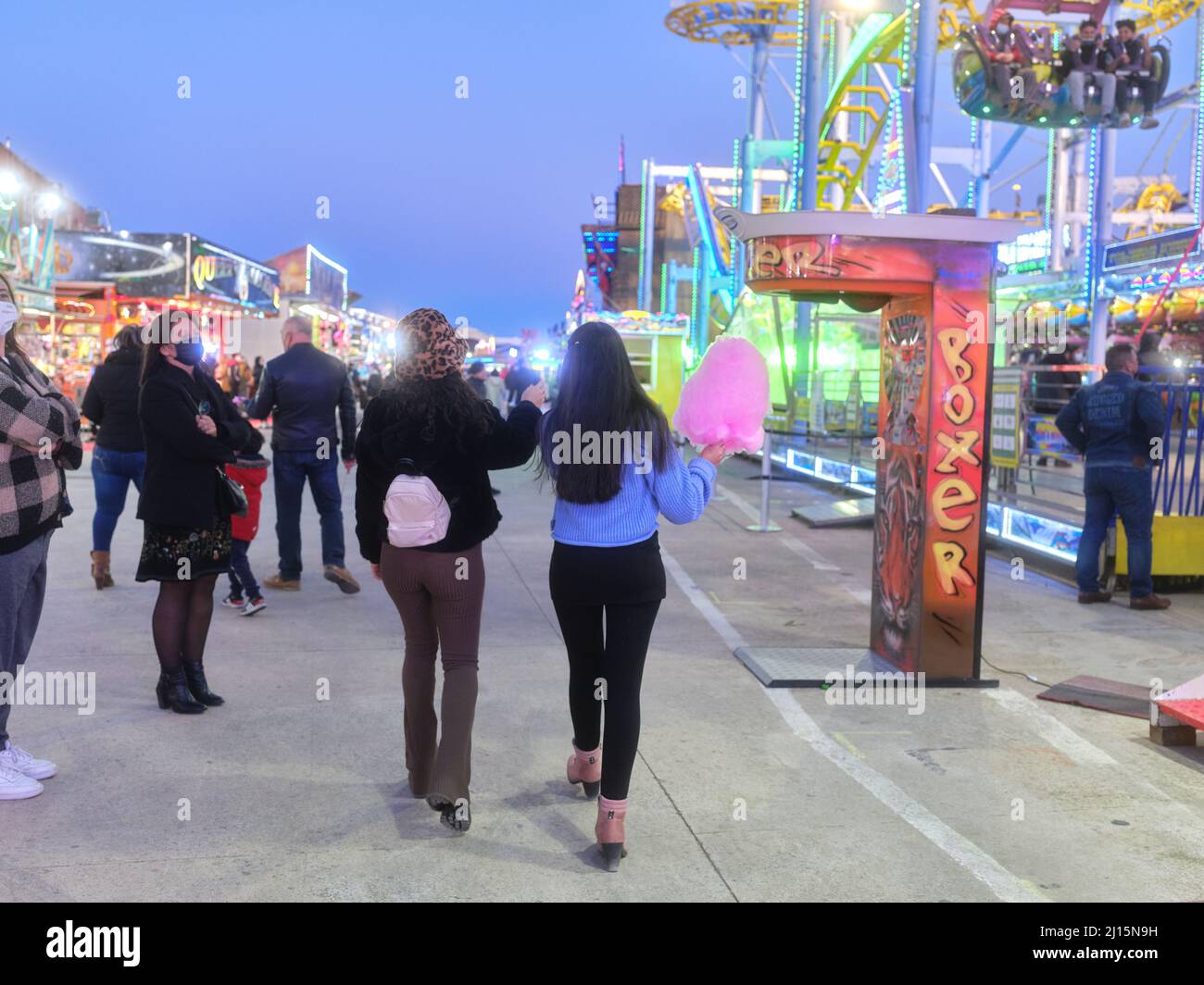 Back of two women strolling while eating a cotton candy at an evening fair Stock Photo