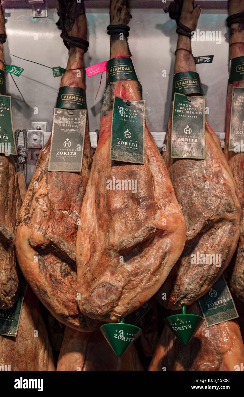 Pamplona, Spain - June 20, 2021: Whole bone-in legs of Spanish serrano iberico ham hanging on display at a butcher shop in the old town or Casco Viejo Stock Photo