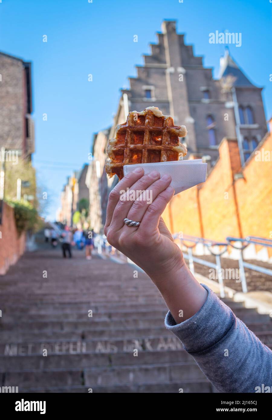 Delicious belgian waffle held in front of blurred background of Montagne de Bueren staircase in Liege, which is a city's top tourist attraction Stock Photo