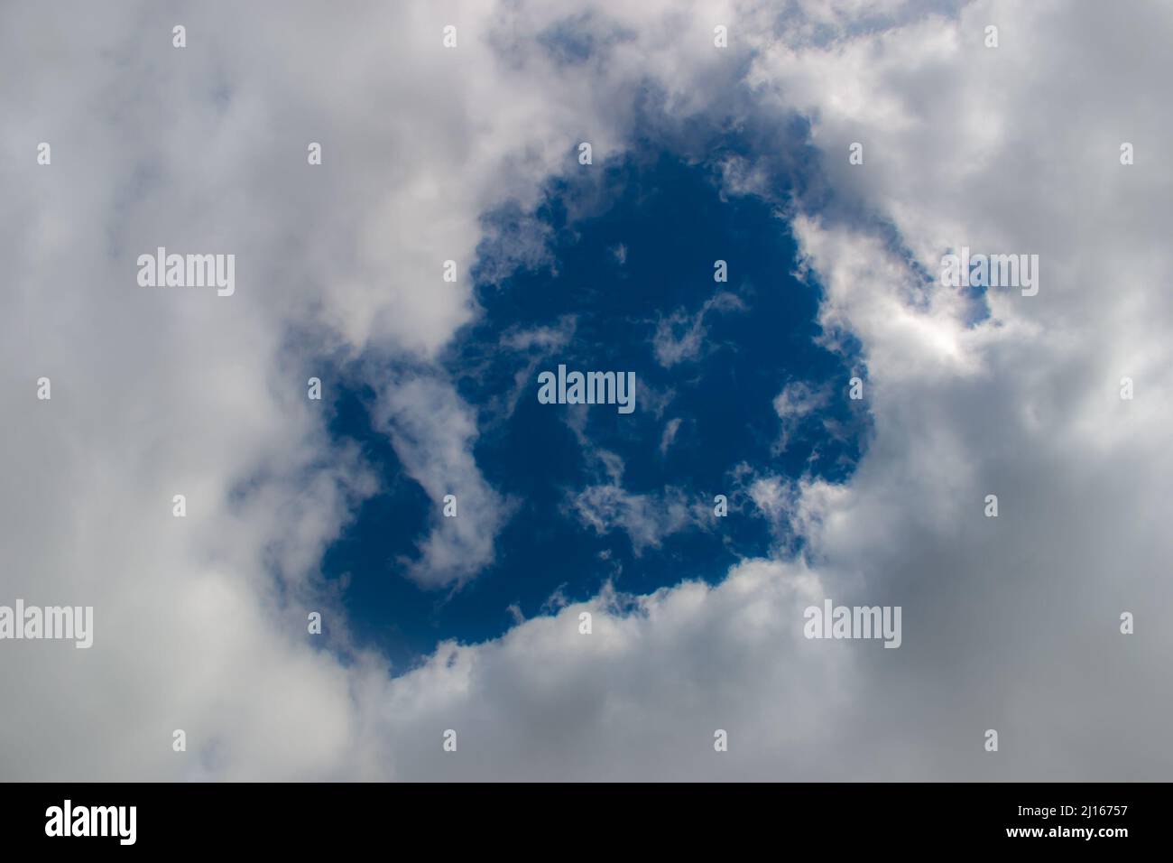 A hole through thick fluffy white clouds showing the deep blue sky behind Stock Photo