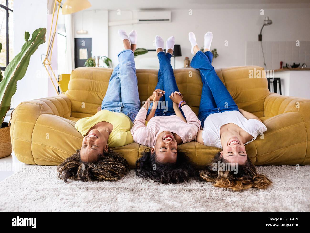 Multiracial best friends laying upside down on sofa and smiling at home Stock Photo
