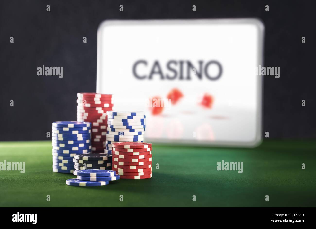 Gambling on internet casino. Online betting with tablet, computer or laptop. Stack of poker chips on green table. Playing digital mobile games. Stock Photo