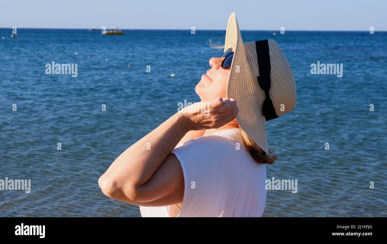 happy 50 year old woman in straw hat and sunglasses enjoying the sun