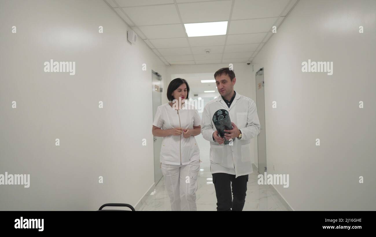 Two doctors walk down corridor and discussing about mri brain scan. Healthcare professional looking x-ray of patient's walking along corridor of Stock Photo