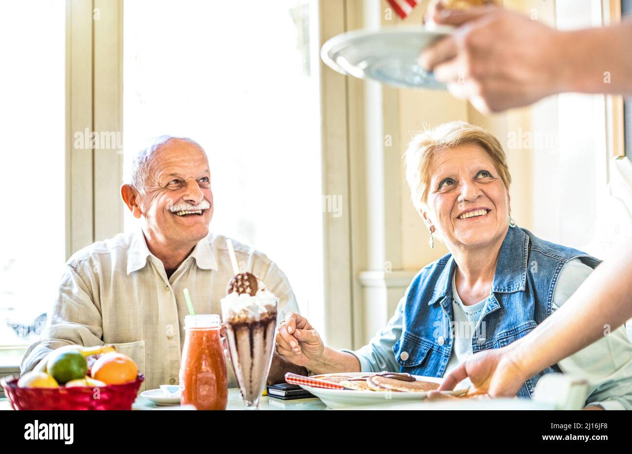 Waiter serving senior retired couple eating cakes at fashion bio restaurant - Pension and active elderly concept with mature people having genuine fun Stock Photo