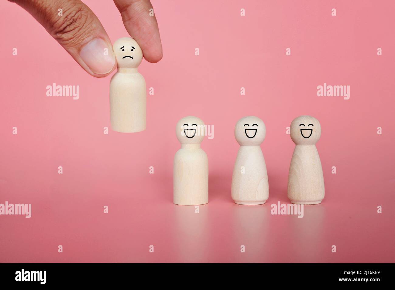 Firing, bad employee and demotion concept. Hand pick wooden doll with sad face icon. Pink background Stock Photo