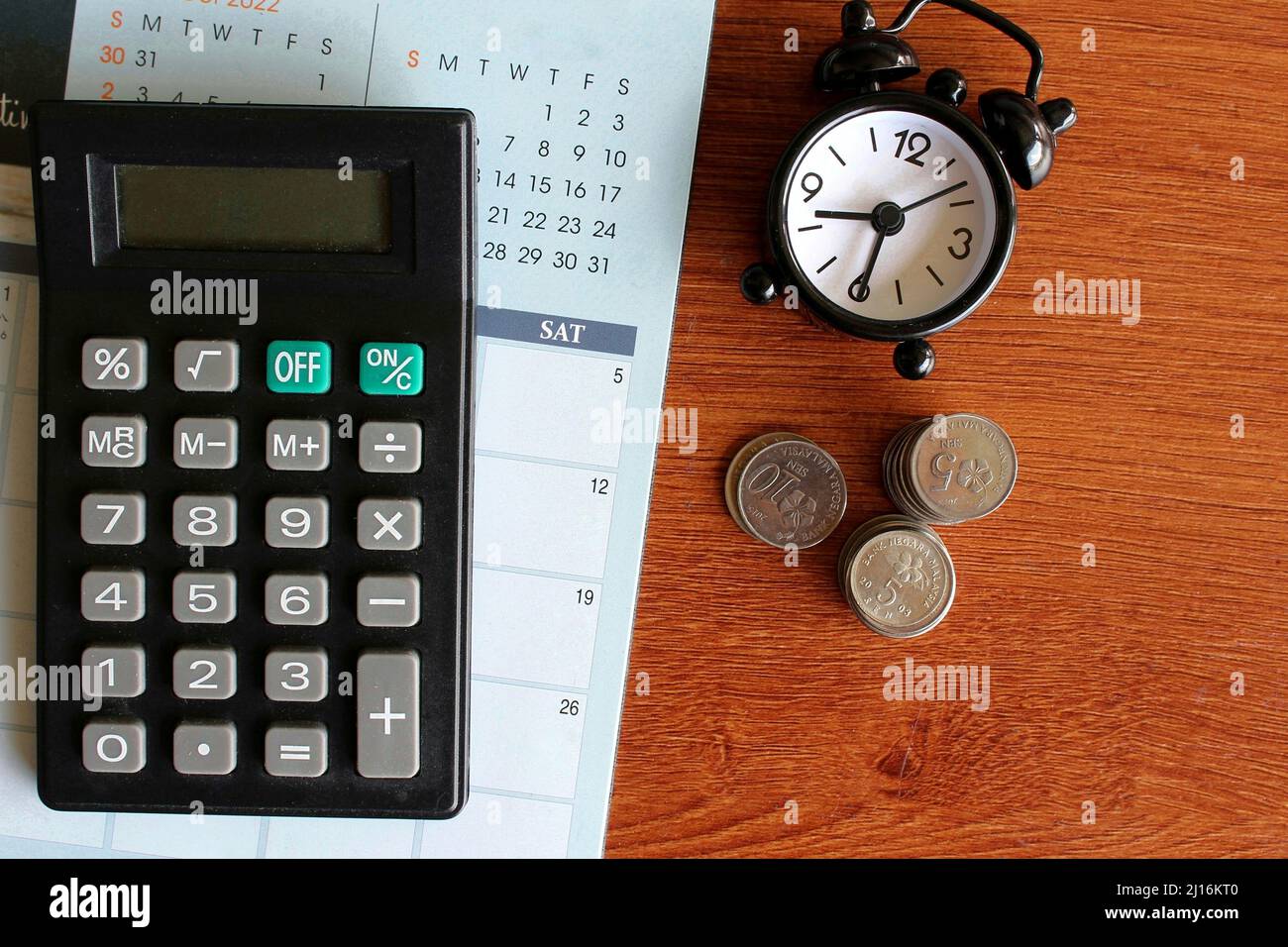 Top view image of calculator, calendar, alarm clock and coins on wooden table. Stock Photo