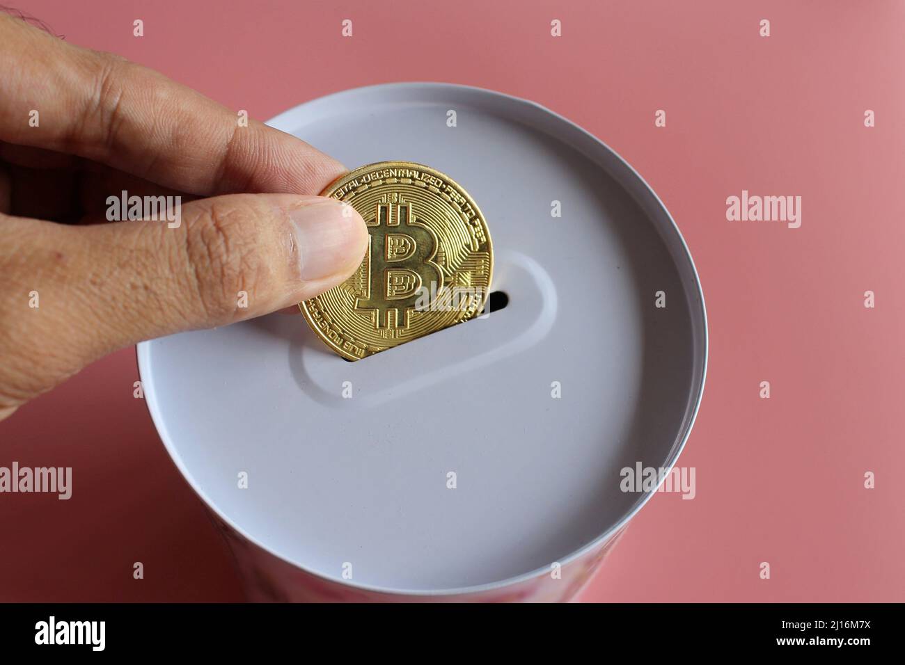 Hand put Bitcoin into donation box. Pink background. Cryptocurrency and donation concept. Stock Photo