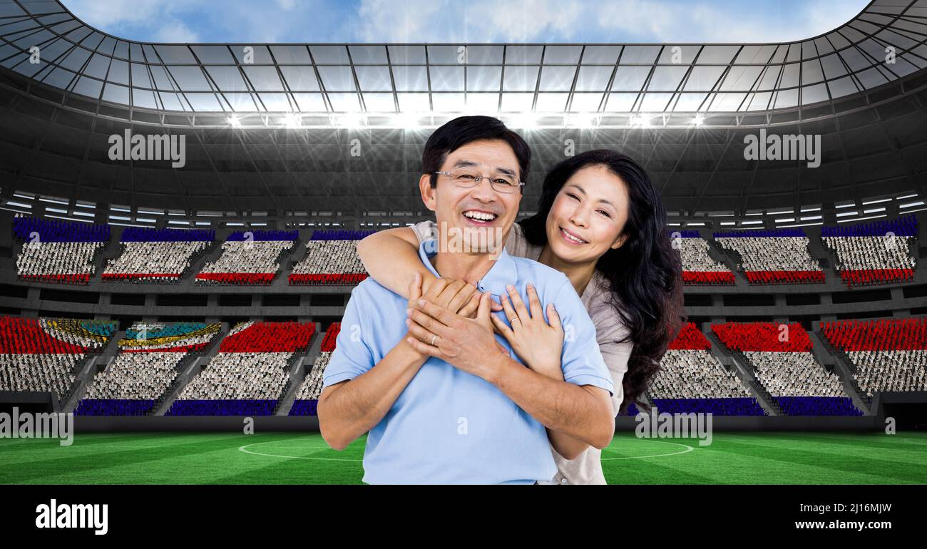 Composite image of asian couple hugging each other against sports stadium Stock Photo