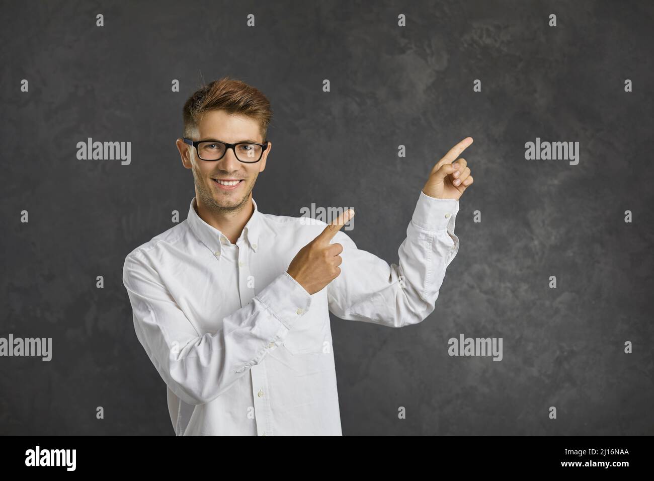 Friendly man with smiling expression points his index fingers to the side on gray background. Stock Photo