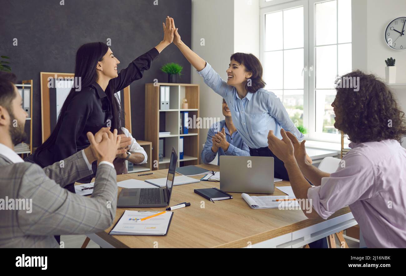 Two happy colleagues giving high five over table in office celebrating ...