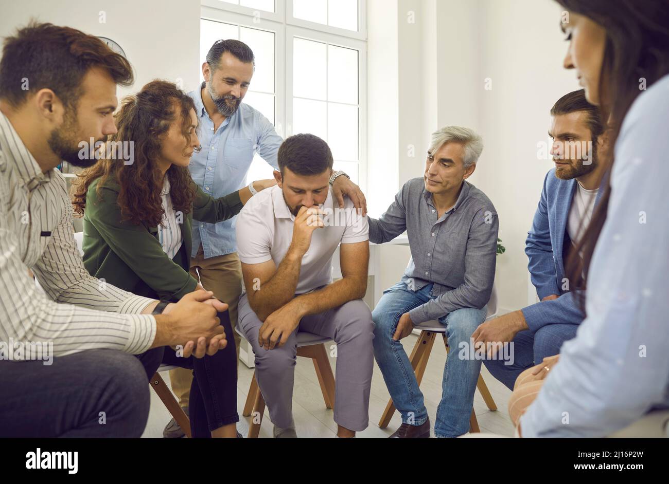 People provide psychological support to a sad male patient during a group therapy session. Stock Photo