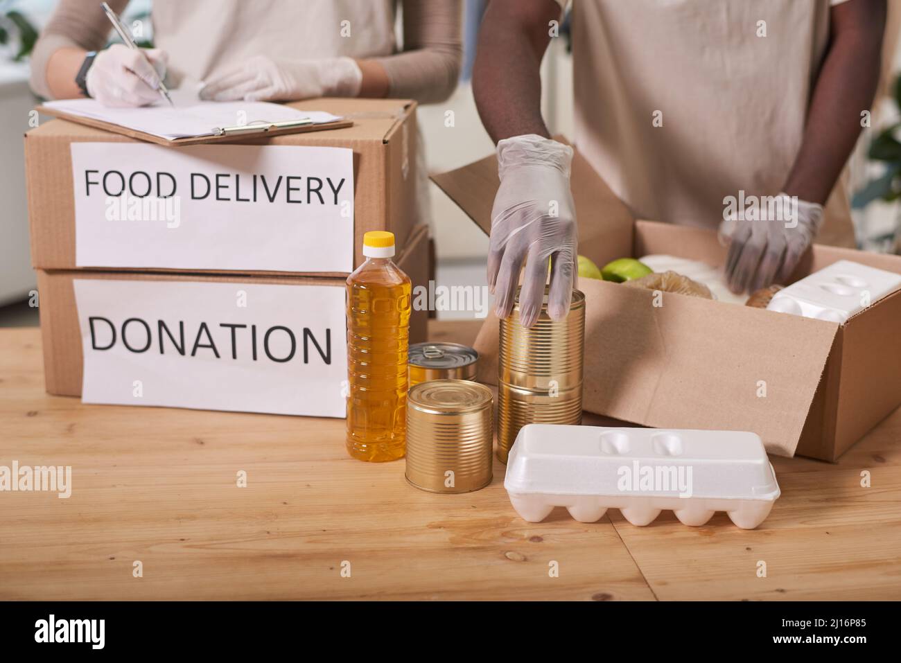 Medium section shot of unrecognizable man and woman wearing latex gloves packing food supplies for donation Stock Photo