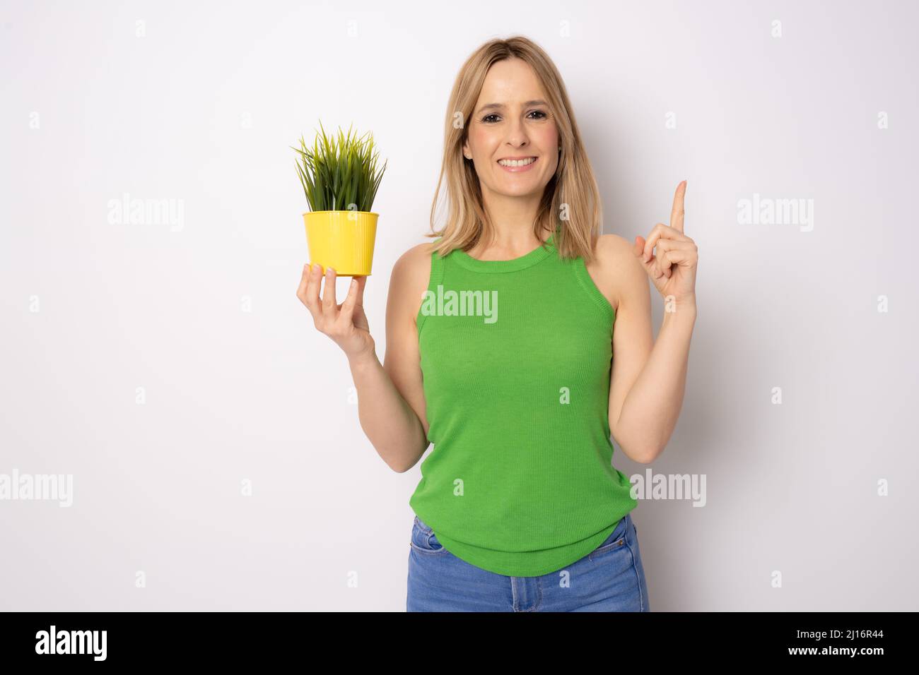 Smiling beautiful young woman in green top is posing with a plant in ...