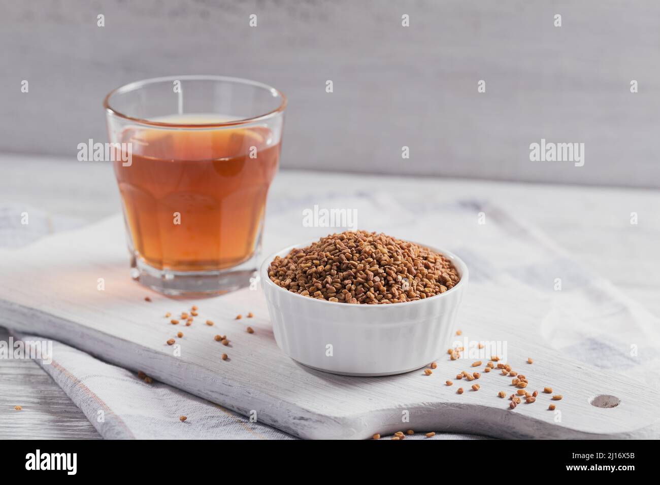 Bowl of fenugreek seeds and Egyptian fenugreek yellow tea or Methi Dana drink on white wooden background Stock Photo