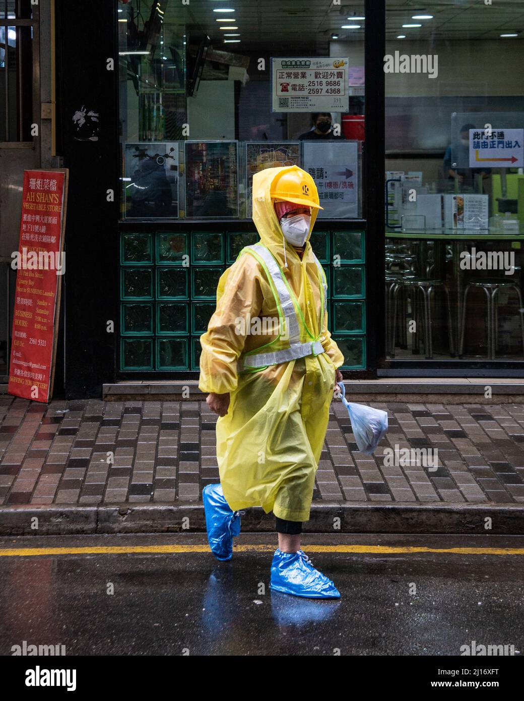 A worker in high-viz gear and a protective mask goes about their daily routine as a northern monsoon brings cooler weather and rain to Hong Kong. A rainy, spring day in Hong Kong. Stock Photo