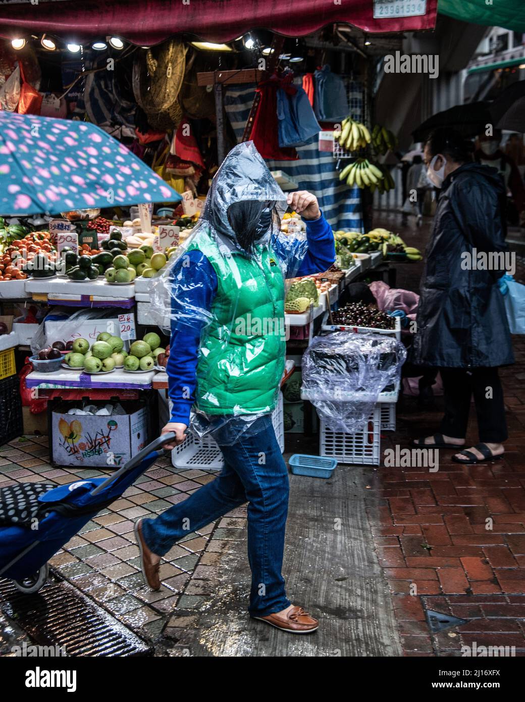 A shopper wearing a raincoat carries his goods from the wet market as a northern monsoon brings cooler weather and rain to Hong Kong. A rainy, spring day in Hong Kong. Stock Photo