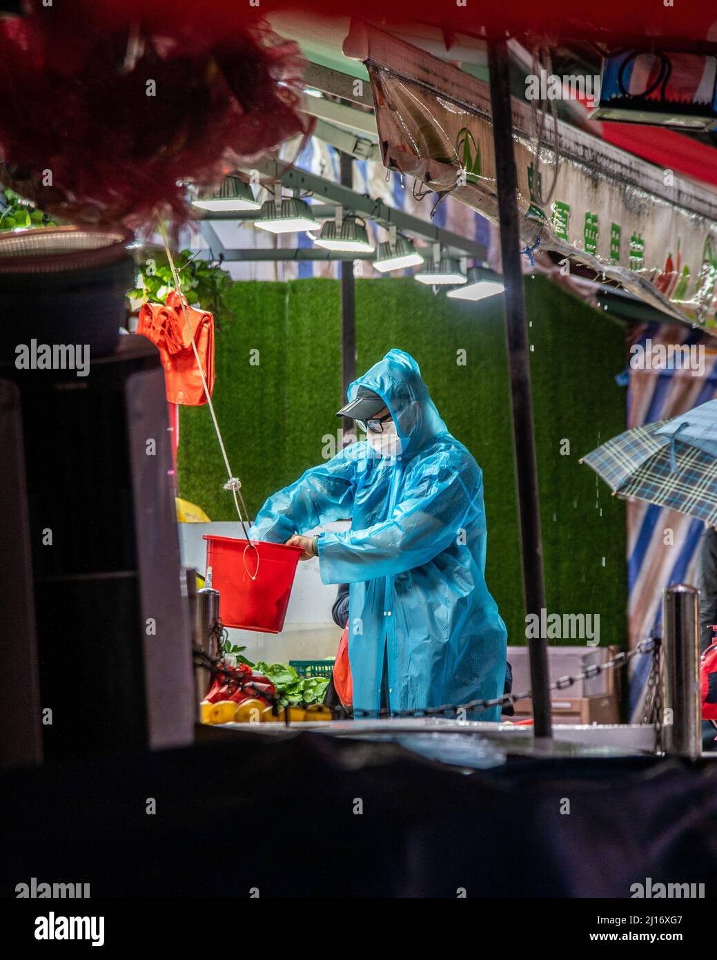 A worker wearing a rain coat grabs change for a customer as a northern monsoon brings cooler weather and rain to Hong Kong. A rainy, spring day in Hong Kong. Stock Photo