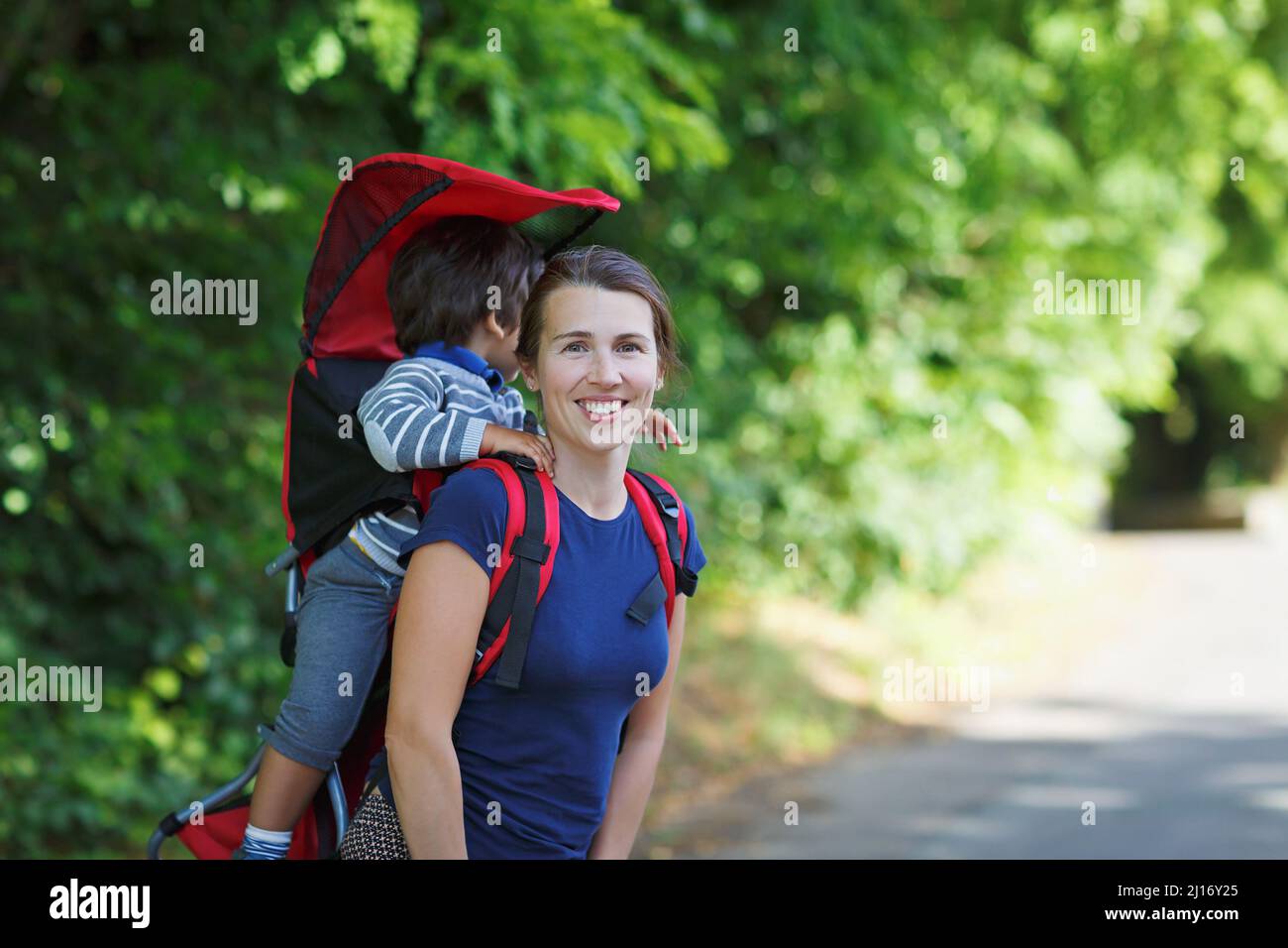 Mother with toddler child in backpack carrier is walking in forest