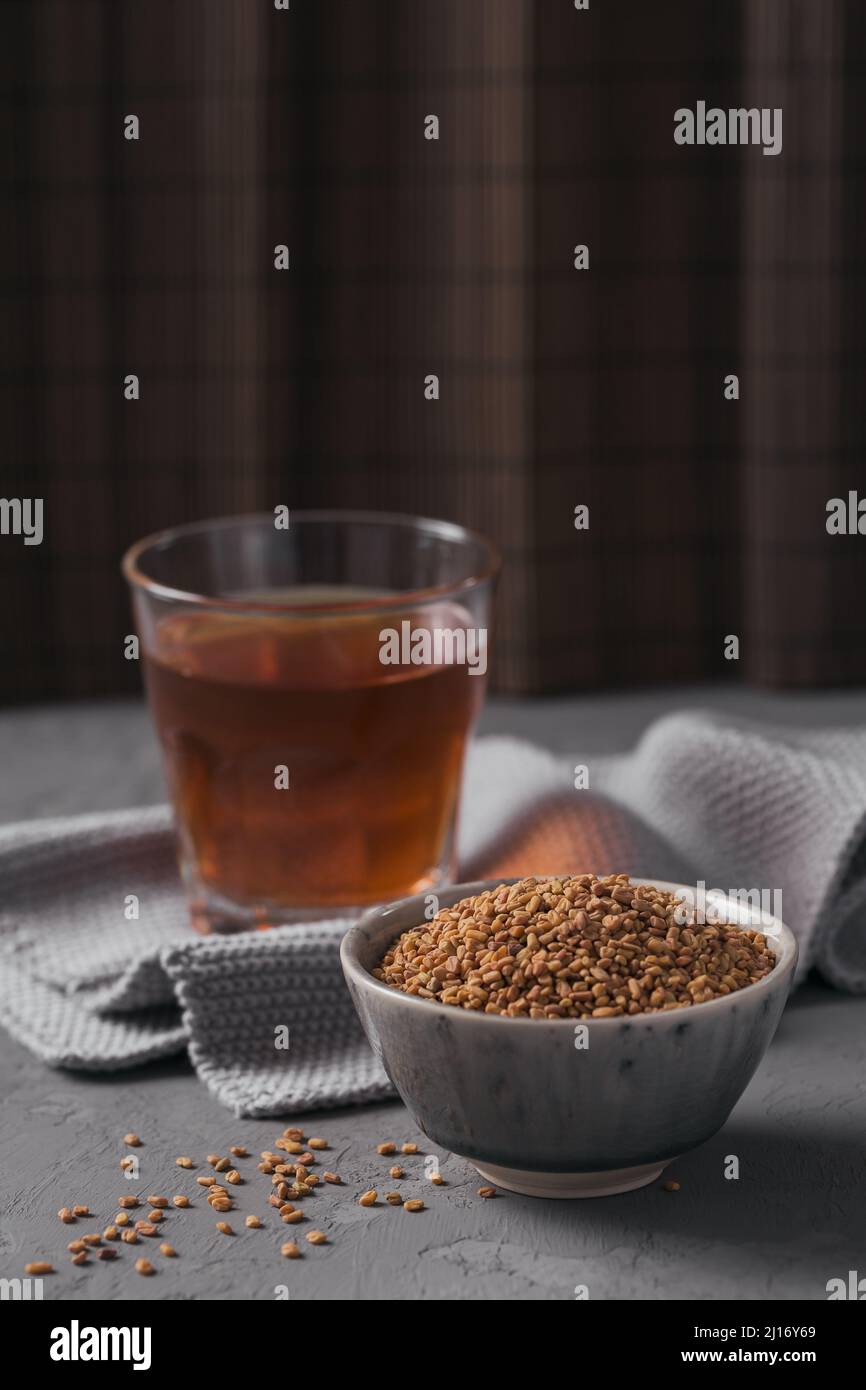 Glass of Egyptian fenugreek yellow tea, Helba or Methi Dana drink and fenugreek seeds on grey background Stock Photo