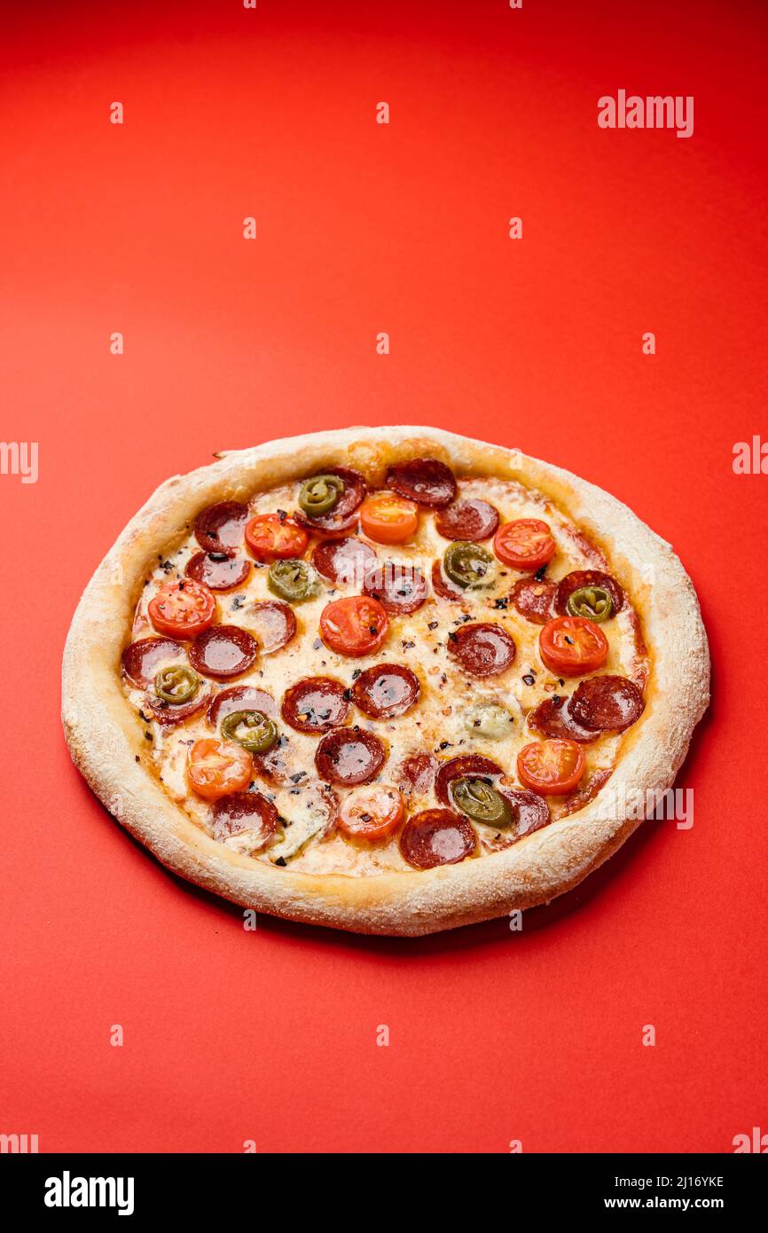 https://c8.alamy.com/comp/2J16YKE/pizza-with-smoked-sausage-cherry-tomatoes-dried-chilli-jalapeno-peppers-and-mozzarella-red-background-copy-space-2J16YKE.jpg