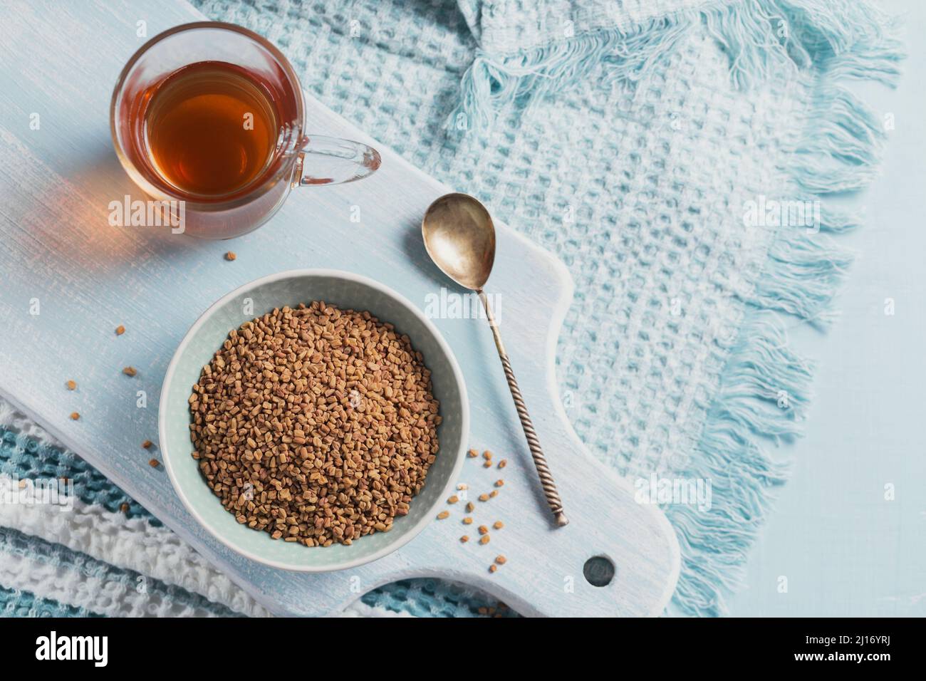 Bowl of fenugreek seeds and Egyptian fenugreek yellow tea or Methi Dana drink on light blue background Stock Photo
