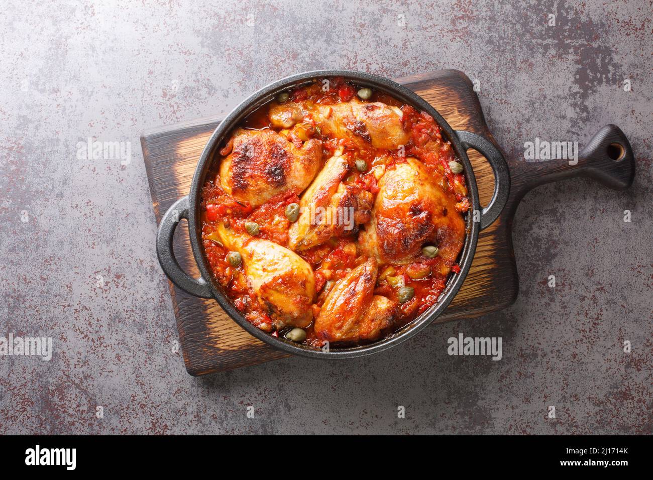 Spanish food chicken baked with tomato, pepper, onion and garlic sauce close-up in a frying pan on a cutting board. horizontal top view from above Stock Photo