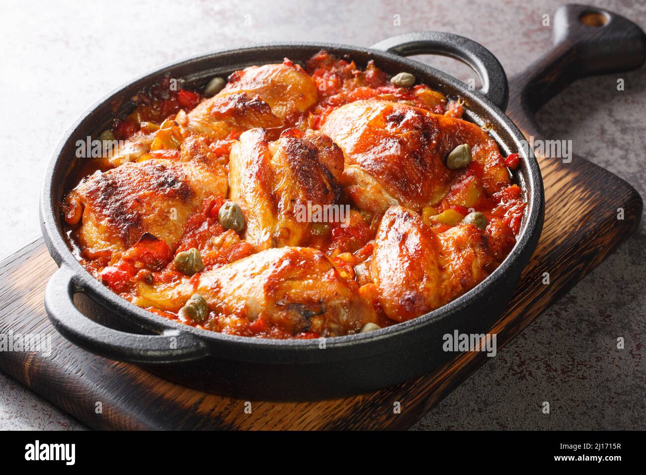 Rustic style chicken baked with a sauce of tomatoes, peppers, onions and garlic close-up in a frying pan on a cutting board. horizontal Stock Photo