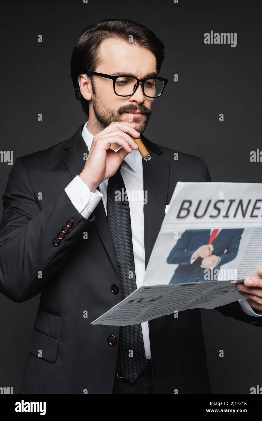 man in suit and glasses reading business newspaper and holding cigar on dark grey Stock Photo