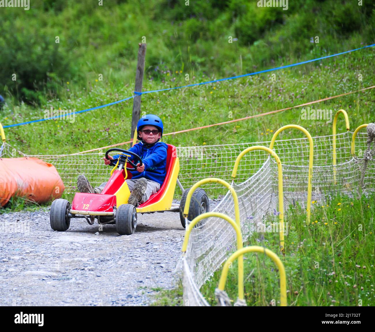 young boy rolling down hill in a go kart in the french alps at super devoluy ,holiday activity ,ski resort in summer . Stock Photo
