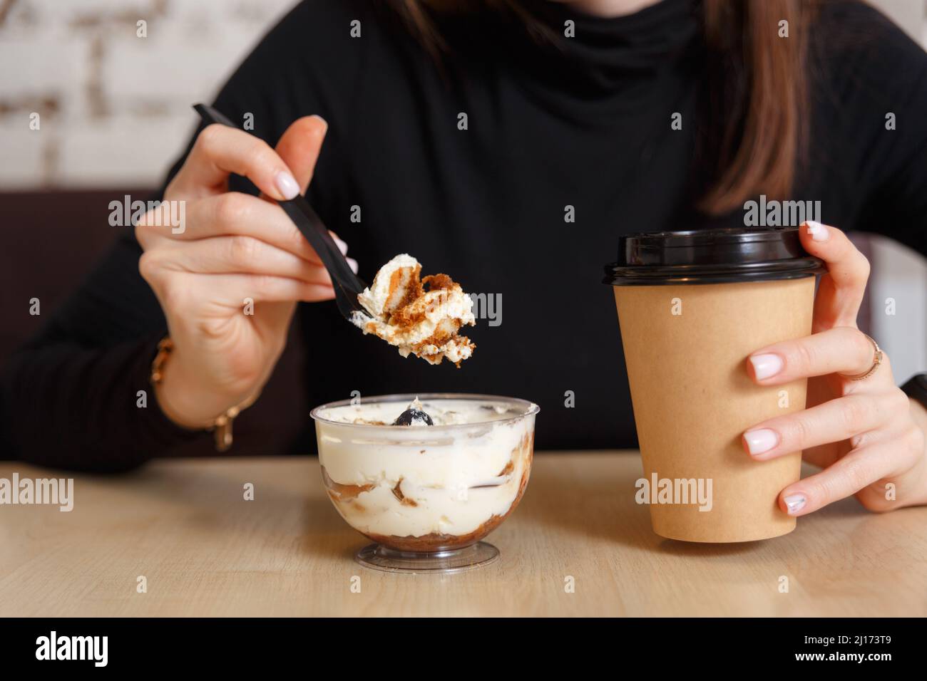Woman eats creamy dessert and drinks coffee at breakfast in cafe. Food