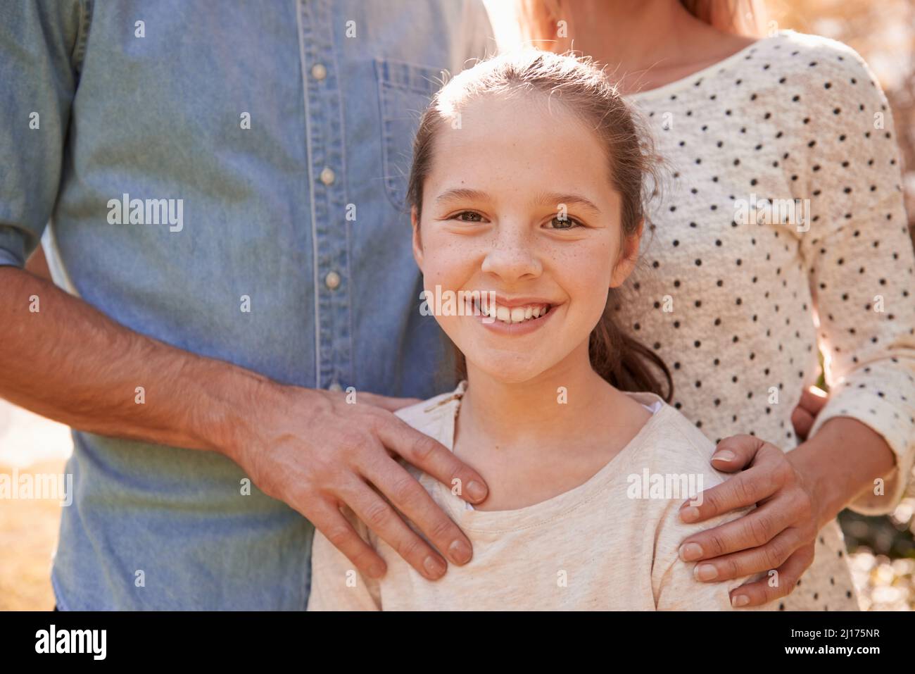 Shes their pride and joy. A cropped portrait of a happy young girl standing outdoors with her parents. Stock Photo